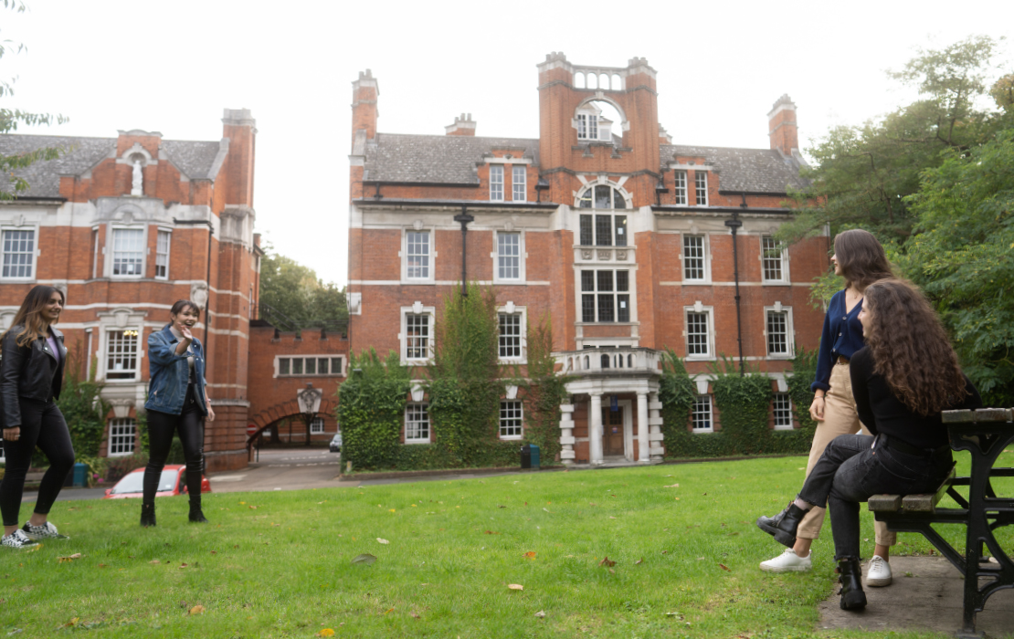Two pairs of students, waving and talking to each other outside building on the Medway campus